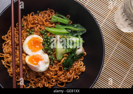 Tagliatelle in nero ciotola guarnendo il piatto sul tavolo da cucina Foto Stock