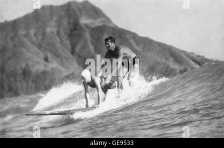 Tom Blake e Odetta Bray tandem surf negli anni trenta a Waikiki a Honolulu, Hawaii con testa di diamante in background. Foto Stock