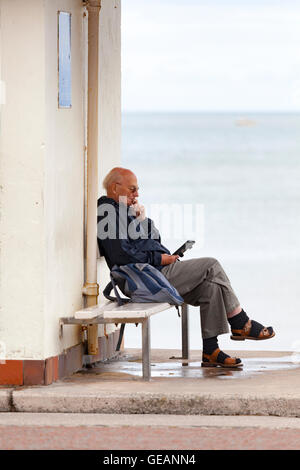 Llandudno, Wales, Regno Unito. Il 25 luglio 2016. Regno Unito - Previsioni del tempo - Un giorno nuvoloso con al di sotto della media di temperatura in corrispondenza della stazione balneare di Llandudno, il Galles del Nord. Nonostante il meteo persone stanno godendo il resort tutto lo stesso. Un uomo godendo di una lettura in uno dei numerosi rifugi sul lungomare lungo la promenade Foto Stock