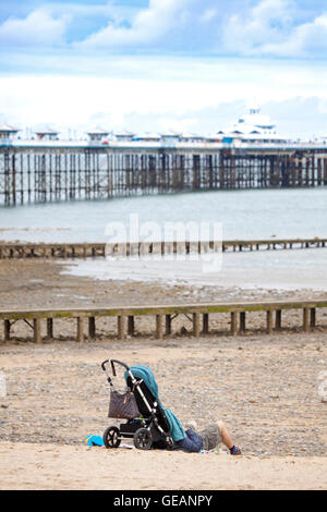 Llandudno, Wales, Regno Unito. Il 25 luglio 2016. Regno Unito - Previsioni del tempo - Un giorno nuvoloso con al di sotto di temperature medie come la stazione balneare di Llandudno, il Galles del Nord. Un padre rilassante sulla spiaggia presso la popolare spiaggia resort Foto Stock