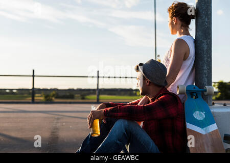 Coppia giovane con lo skateboard e bottiglia di birra godendo del tramonto Foto Stock