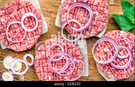 Terra cruda carni bovine cotoletta per fare gli hamburger con anelli di cipolla e spezie su sfondo di legno Foto Stock