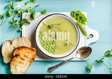 Luce estate pisello verde minestra di crema nella ciotola con i germogli di crostini di pane e spezie Foto Stock