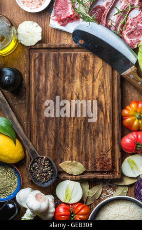 Ingredienti per la cottura della carne sana la cena. Materie non cotti costolette di agnello con verdure, riso, erbe aromatiche e spezie su legno rustico sfondo scuro, tagliere in centro Foto Stock