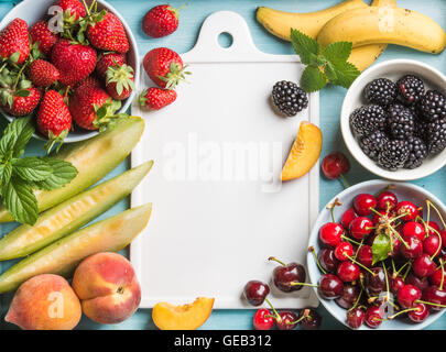 Una sana frutta estiva varietà. Ciliegie dolci, fragole, more, pesche, banane, fette di melone e foglie di menta blu su sfondo bianco con bordo in ceramica nel centro Foto Stock