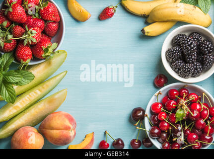 Una sana frutta estiva varietà. Ciliegie dolci, fragole, more, pesche, banane, fette di melone e foglie di menta su sfondo blu Foto Stock