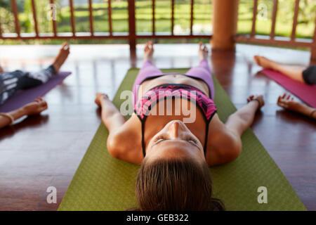 Immagine ravvicinata di giovani donne che giace sul tappeto di esercizio in corso di yoga. Giovani rilassante in savasana posa al club della salute. Foto Stock