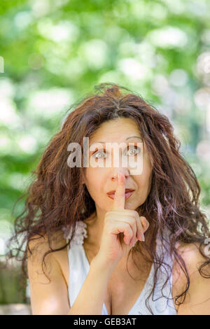 Donna elegante mettere il dito indice alle labbra per silenzio in un giardino Foto Stock