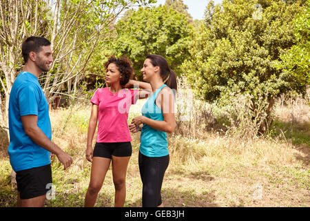 Tre giovani felici gli amanti del jogging prendendo una pausa all'ombra degli alberi nella tarda mattinata di indossare magliette e pantaloni neri Foto Stock