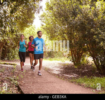 Un maschio e femmina di due amici in esecuzione su di un sentiero per jogging circondato da alberi in tarda mattinata le ombre che indossa la t-shirt e bl Foto Stock