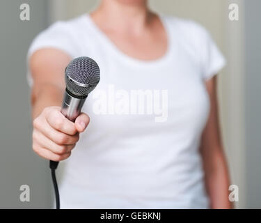 Close up della donna in maglia bianca, che offre a qualcuno di darle un'intervista. Tenendo il microfono in mano. Foto Stock