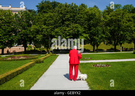 Un uomo vestito di rosso a piedi un cane bianco in un parco Foto Stock