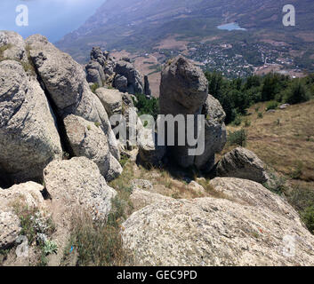 Colonne in pietra sotto forma di strati di lava sopra la valle e il villaggio. Crimea Foto Stock