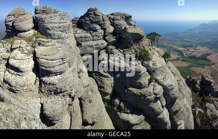 Colonne in pietra sotto forma di strati di lava sopra la valle e il villaggio. Crimea Foto Stock