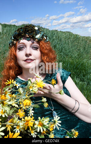 Bella giovane donna con lunghi, ricci capelli rossi che indossa il verde e l'azienda fiori gialli. Foto Stock