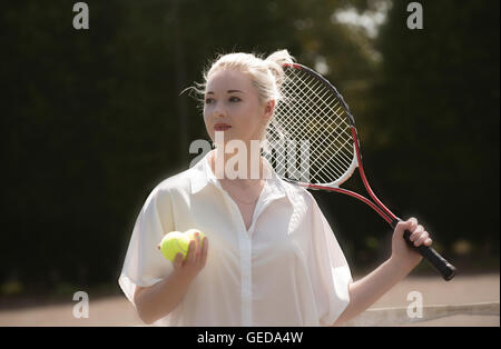 Ritratto di un giovane giocatore di tennis. Una femmina giovane giocatore di tennis con capelli biondi tenendo un racchette e palle da tennis Foto Stock