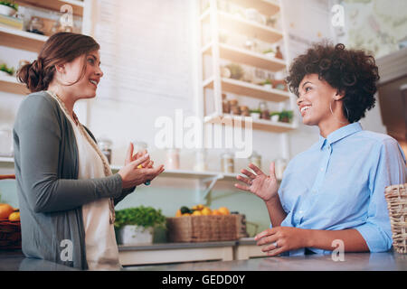 Due felice femmina giovane cameriera in piedi dietro un banco di bar di parlarsi. Juice Bar partner per discutere di nuovi affari. Foto Stock