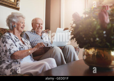 Ritratto di sorridente coppia senior seduti insieme a casa e navigare in Internet sul computer portatile. Il vecchio uomo e donna relax su un divano Foto Stock