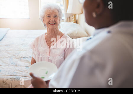 Piscina colpo di senior donna seduta sul letto e home care nurse dando farmaco. Anziani caucasica donna sorridente. Foto Stock