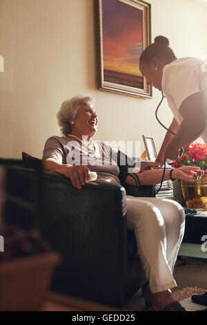 Home operatore sanitario a misurare la pressione del sangue del paziente anziano a casa. Femmina lavoratore healthcare facendo checkup di routine di un anziano p Foto Stock