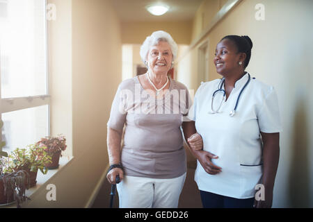 Felice lavoratore del settore sanitario e senior donna insieme presso la casa di cura. La cura medico donna assistere un paziente senior a camminare. Foto Stock
