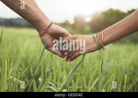 Colpo di coppia romantica tenendo le mani in un campo. Immagine ravvicinata di un uomo e di una donna con la mano nella mano a piedi attraverso il campo di erba. Foto Stock