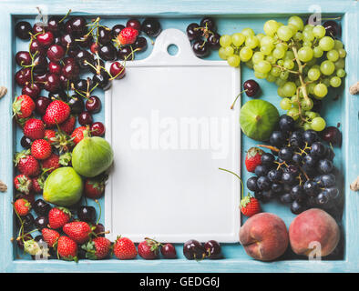 Una sana frutta estiva varietà. Figg, nero e verde uva, le ciliege, le fragole, pesche su blu in legno dipinto con sfondo bianco di ceramica pensione in centro, spazio di copia Foto Stock