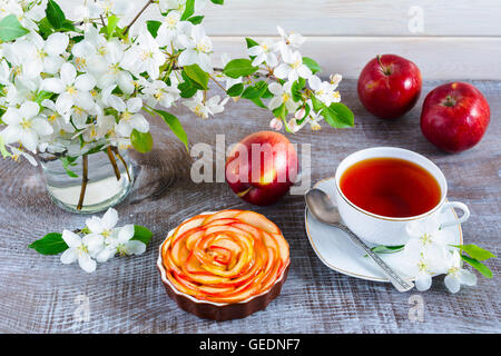 Apple a forma di rosa torta e tazza di tè sul tavolo di legno. In casa torta di mele per il tè in tempo. Colazione tè con dolci di pasticceria di apple. Foto Stock