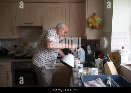 La vecchiaia pensionato rendendo tazze di tè per i visitatori nella sua cucina a casa in Inghilterra, Regno Unito Foto Stock