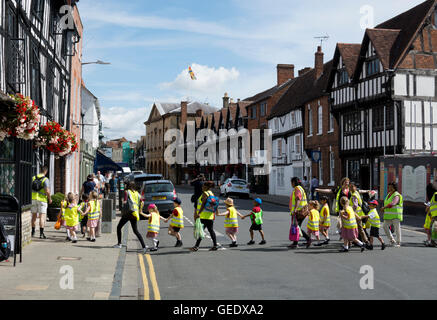 I bambini in alta visibilità gilet essendo portato attraverso una Street, Stratford-upon-Avon, Regno Unito Foto Stock