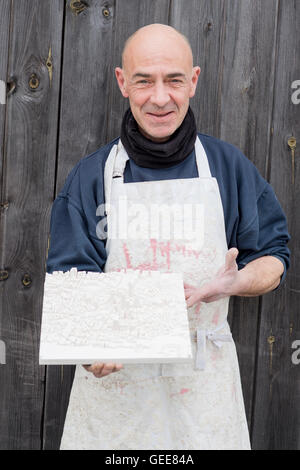 Uomo in abbigliamento spessa e grembiule bianco presentando un modello 3D di una mappa della città in gesso Foto Stock