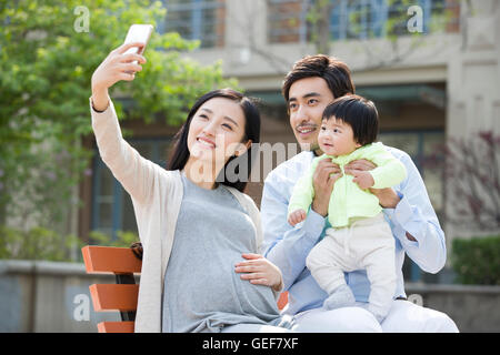 Felice giovane famiglia cinese tenendo autoritratto con uno smart phone Foto Stock