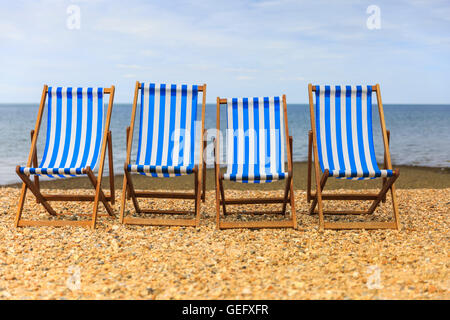 Fila di vuoto quattro sedie a sdraio sulla spiaggia di ghiaia sul soleggiato mare nel Kent, Regno Unito Foto Stock