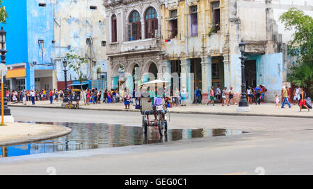 Bicitaxi si trasforma in una strada nel centro del distretto di La Habana, persone in attesa per gli autobus in background, Havana, Cuba Foto Stock