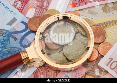 Lente di ingrandimento e le banconote in euro con monete. Il concetto di crisi. Foto Stock