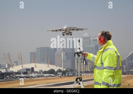 Un ingegnere ambientale controlla i livelli di rumore all'Aeroporto di London City come piano prende il largo. Canary Wharf in background. Foto Stock