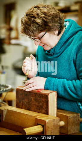 Una donna che lavorano sul dorso di un libro rilegato con un attrezzo a mano. Foto Stock