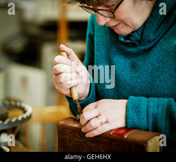 Una donna che lavorano sul dorso di un libro rilegato con un attrezzo a mano. Foto Stock