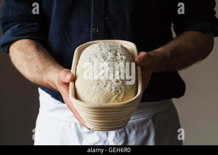 Close up di un fornaio tenendo un pane appena sfornato pagnotta di pane bianco in rattan proofing cestello. Foto Stock