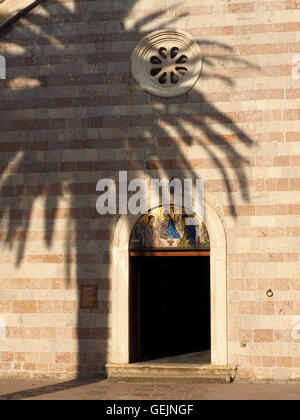 Ombra di Palm tree sulla Chiesa Ortodossa porta con mosaici di icona nel pannello arcuato sopra porta aperta in Budva Old Town Montenegro Foto Stock