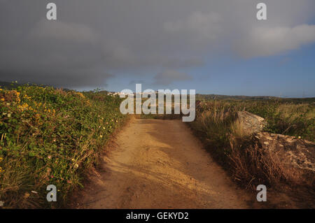 Strada sterrata con nuvole temporalesche avvicinando avanti da est mentre il sole tramonta ad ovest. Foto Stock