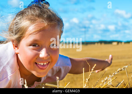 Carino giovane ragazza divertirsi sul pagliaio. Pile di paglia - balle di fieno e laminati in pile a sinistra dopo la mietitura del grano orecchie, Foto Stock