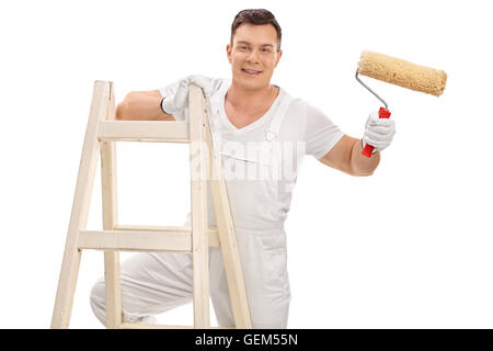 Studio shot di un allegro giovane arredatore tenendo un rullo di vernice e in piedi su una scala isolati su sfondo bianco Foto Stock