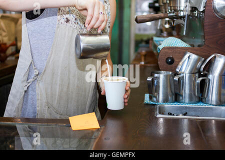 Barista versa latte vaporizzato in un takeaway tazza di caffè in un bar di Melbourne Foto Stock