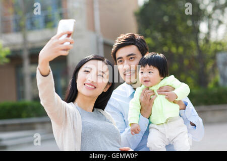 Felice giovane famiglia cinese tenendo autoritratto con uno smart phone Foto Stock