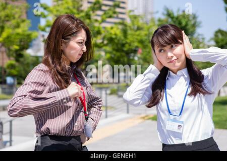 Una donna d'affari essendo arrabbiato e l'altra donna che copre le sue orecchie Foto Stock