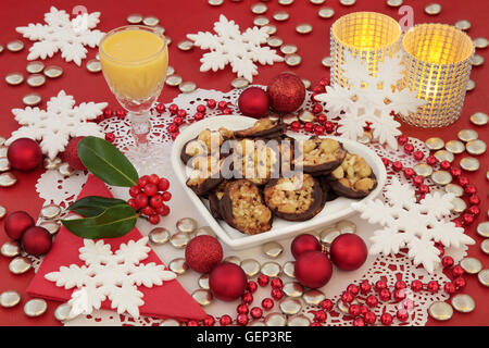 Scena di natale di biscotti Fiorentino su un cuore piastra sagomata, zabaione, agrifoglio, candele e ninnolo decorazioni con i fiocchi di neve. Foto Stock