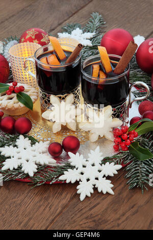 Natale vin brulè, biscotti di panpepato, il simbolo del fiocco di neve e il rosso ninnolo decorazioni, candele, agrifoglio e coperto di neve su fir oak Foto Stock