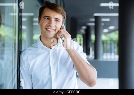 Felice giovane imprenditore in piedi e parlando al cellulare Foto Stock