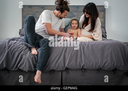 Una coppia giovane e il loro giovane figlio seduti insieme sul loro letto. Foto Stock